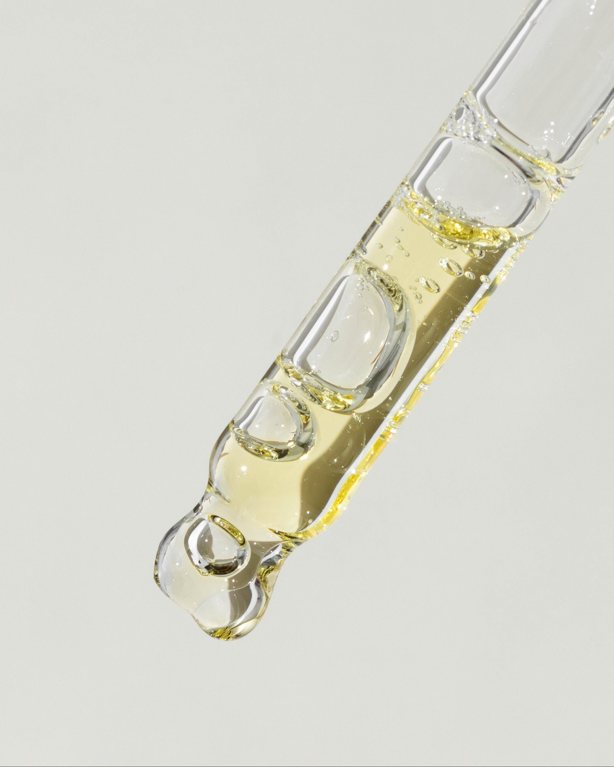 Glass dropper with a clear liquid on a light gray background
